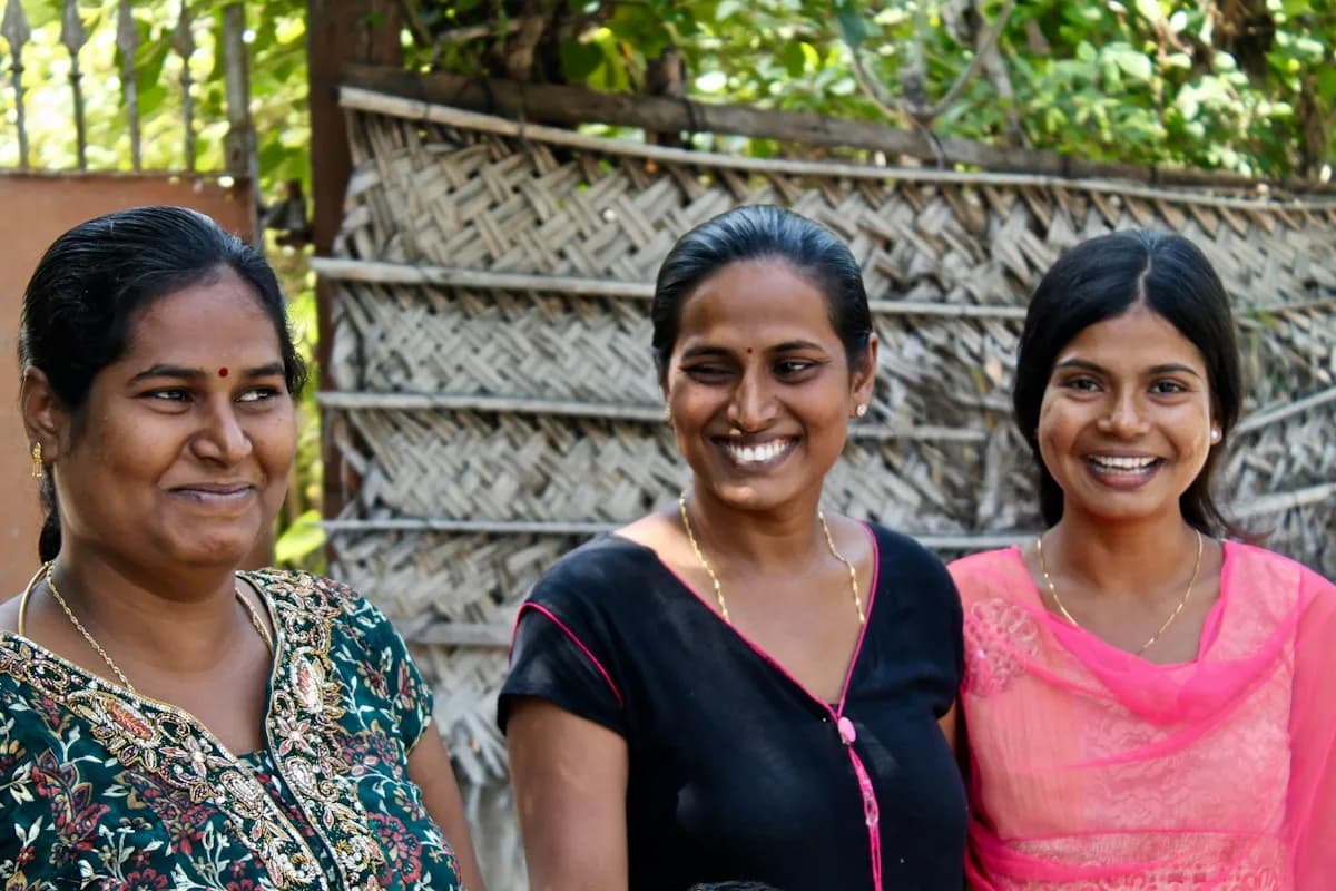 Drei lächelnde Frauen vor einer geflochtenen Bambuswand in Sri Lanka
